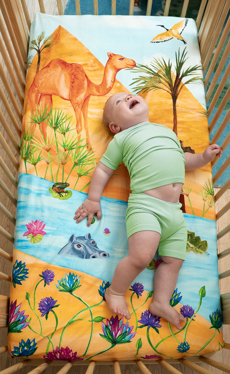 US standard size crib sheet, Naptime on the Nile. Watercolor design featuring the Egyptian pyramids, Nile river, palm trees, sand dunes, camels, lotus flowers, reeds, a crocodile, hippo, lily pads, and a frog.