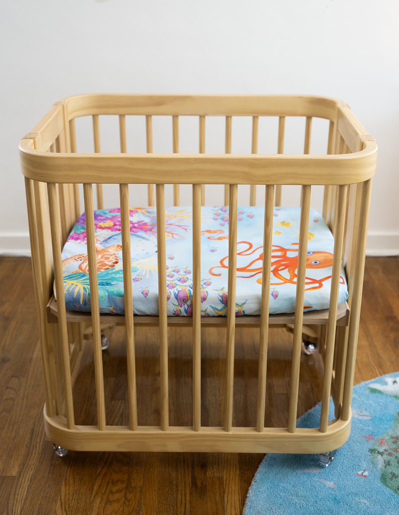 a wide shot showing the entire nestig mini crib with our Sea You In My Dreams sheet on the mattress