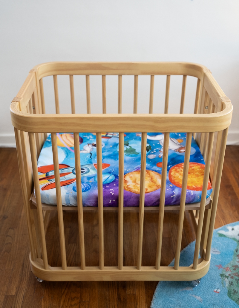 a wide shot showing the entire nestig mini crib with our Barkside of the Moon sheet on the mattress