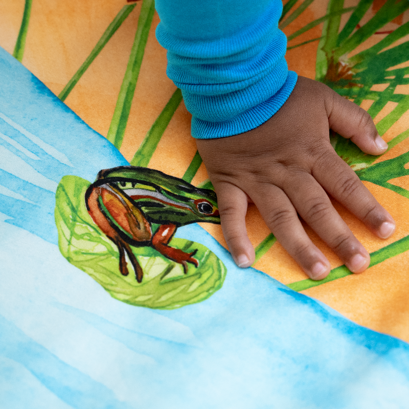 close up of Naptime on the Nile crib sheet showing a watercolored frog sitting on a lily pad that is floating on the nile river.