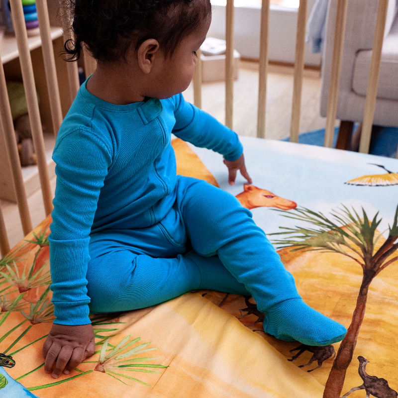 toddler sitting on top of Naptime on the Nile crib sheet pointing at the illustration of a camel.