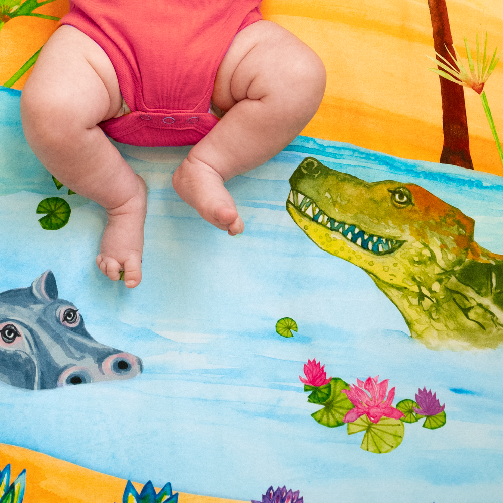 Detail of Naptime on the Nile crib sheet showing a close up of a smiling crocodile, wading hippo, and lily pads floating in the nile river.