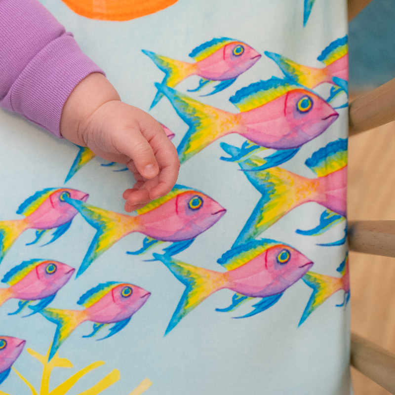 Detail of Sea You In My Dreams crib sheet showing a school of pink, yellow, and blue tropical fish. Ocean crib sheet, 100% cotton crib sheet.