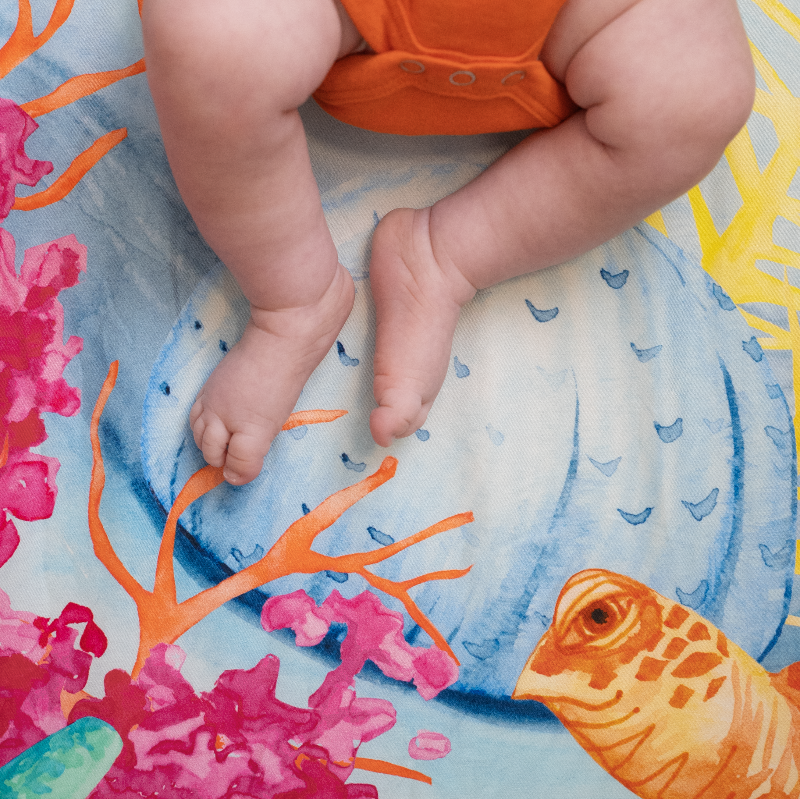 Detail of Sea You In My dreams crib sheet showing a watercolor illustration of a friendly sea turtle's head and pink and orange coral reefs. Ocean crib sheet, 100% cotton crib sheet.