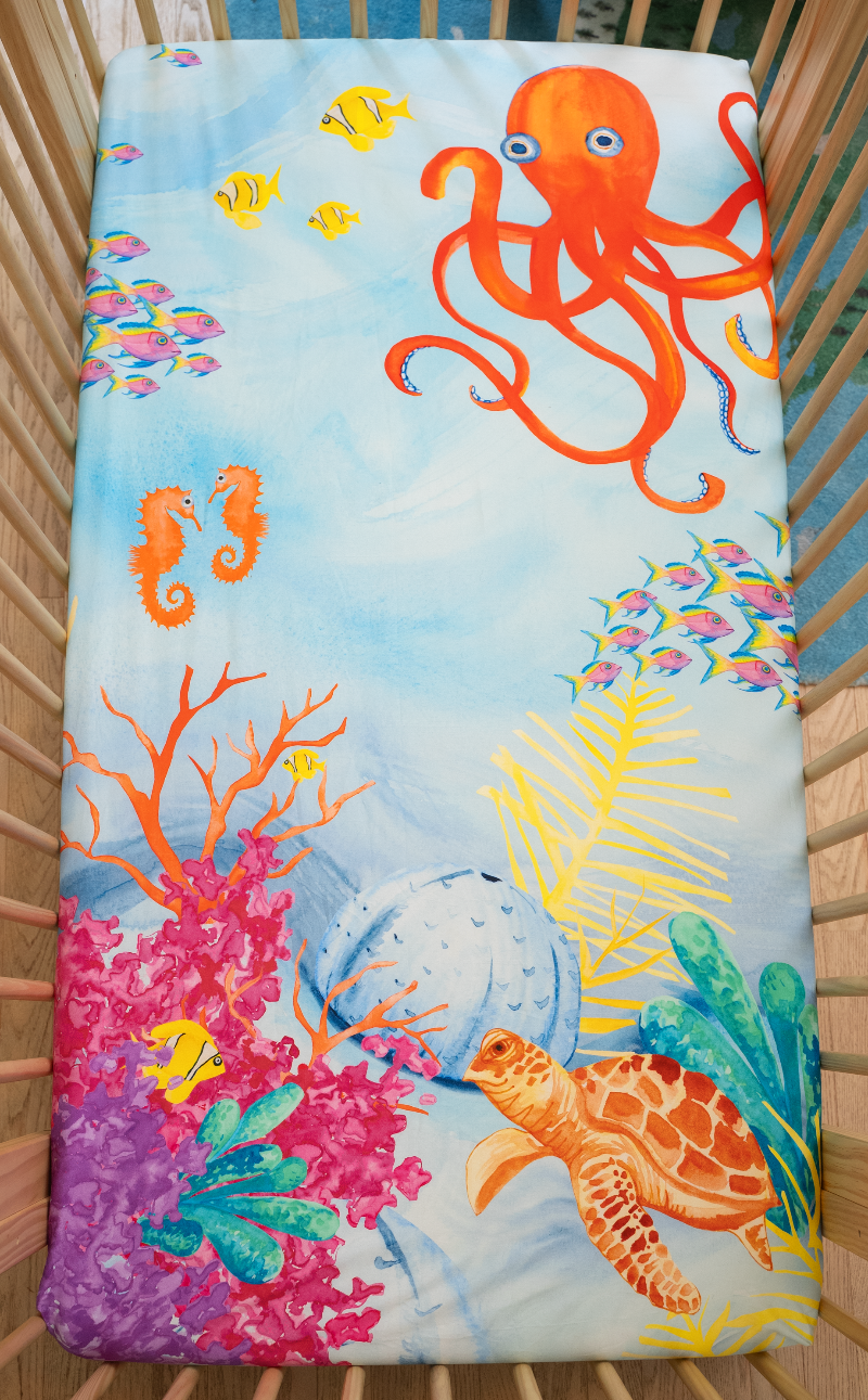 US standard size crib sheet, ocean crib sheet, 100% cotton crib sheet, Sea You In My Dreams. Watercolor design features sea creatures such as a big red-orange octopus, tropical fish, vibrant colored coral, and a friendly sea turtle.