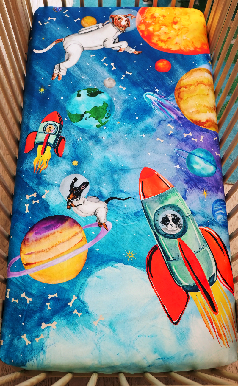 US standard size crib sheet, outer space theme crib sheet that features hand watercolored design of astronaut dogs floating in outer-space surrounded by the solar system, floating bones, and stars. 100% cotton crib sheet.