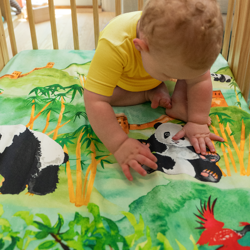 Baby sitting on top of panda crib sheet and looking closely at the painting of the panda.